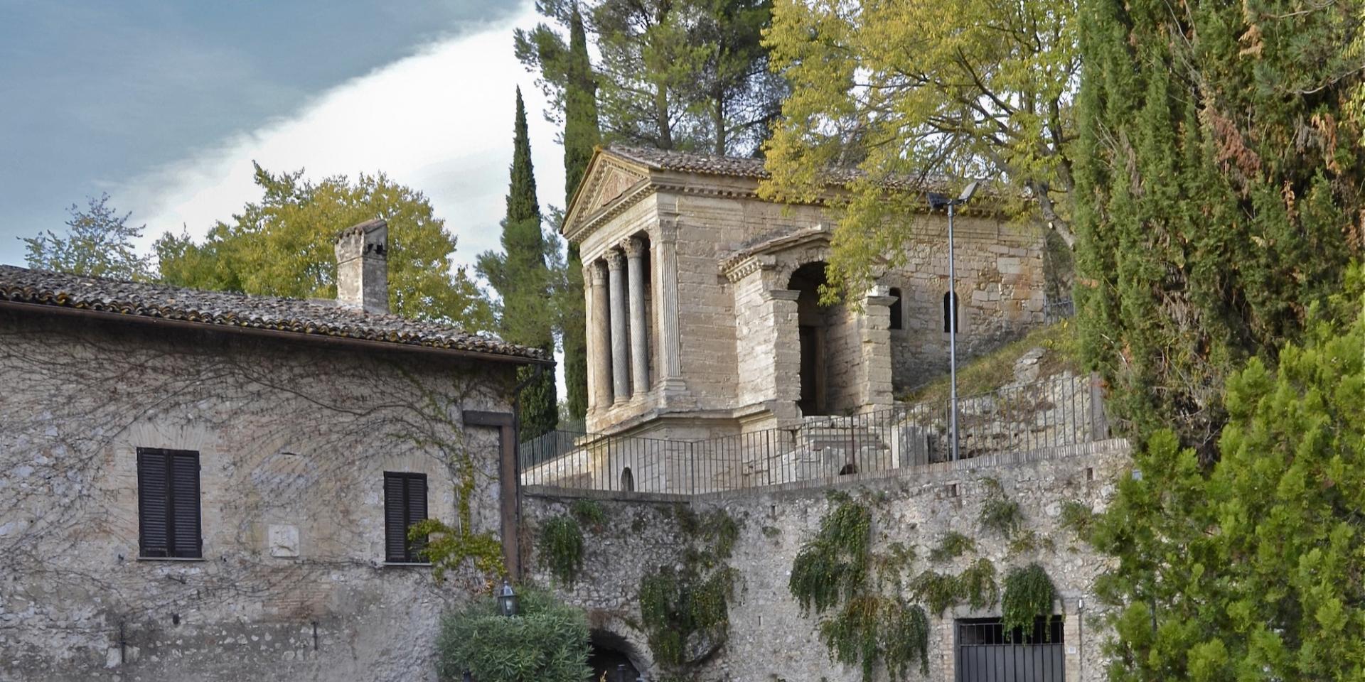The Tempietto del Clitunno, a Lombard-era temple-shaped building with columns and a pediment, nestled in the greenery of the Umbrian countryside